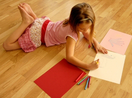 young girl laying on laminate floor while drawing