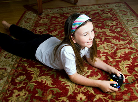 young girl laying on area rug playing a video game